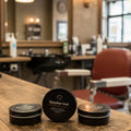 Three small containers of Egyptian God grooming product on a wooden counter with a barbershop background.